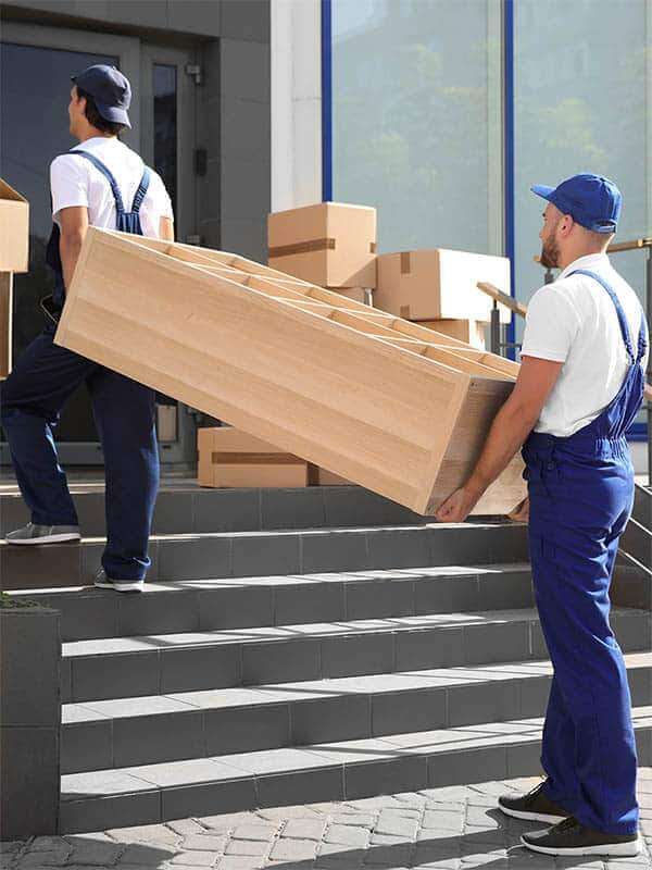 Zwei Umzugshelfer tragen zusammen einen Regal die Eingangstreppe hinauf. - Umzug Kosten - Umzugschecker
