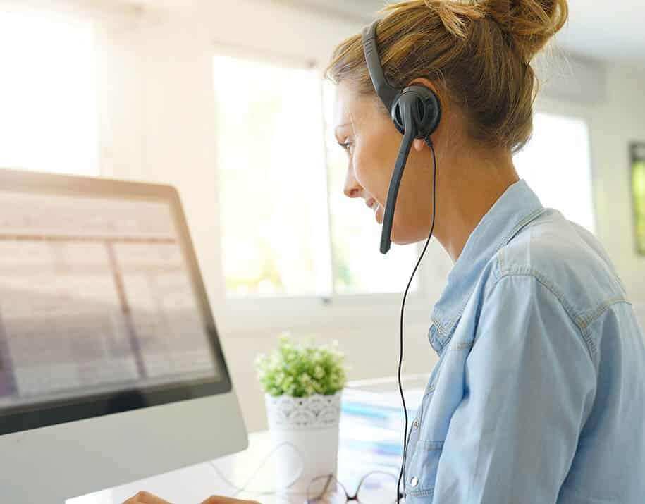 Frau mit Headset schaut im Büro lächelnd auf ihren Bildschirm. - Umzugschecker